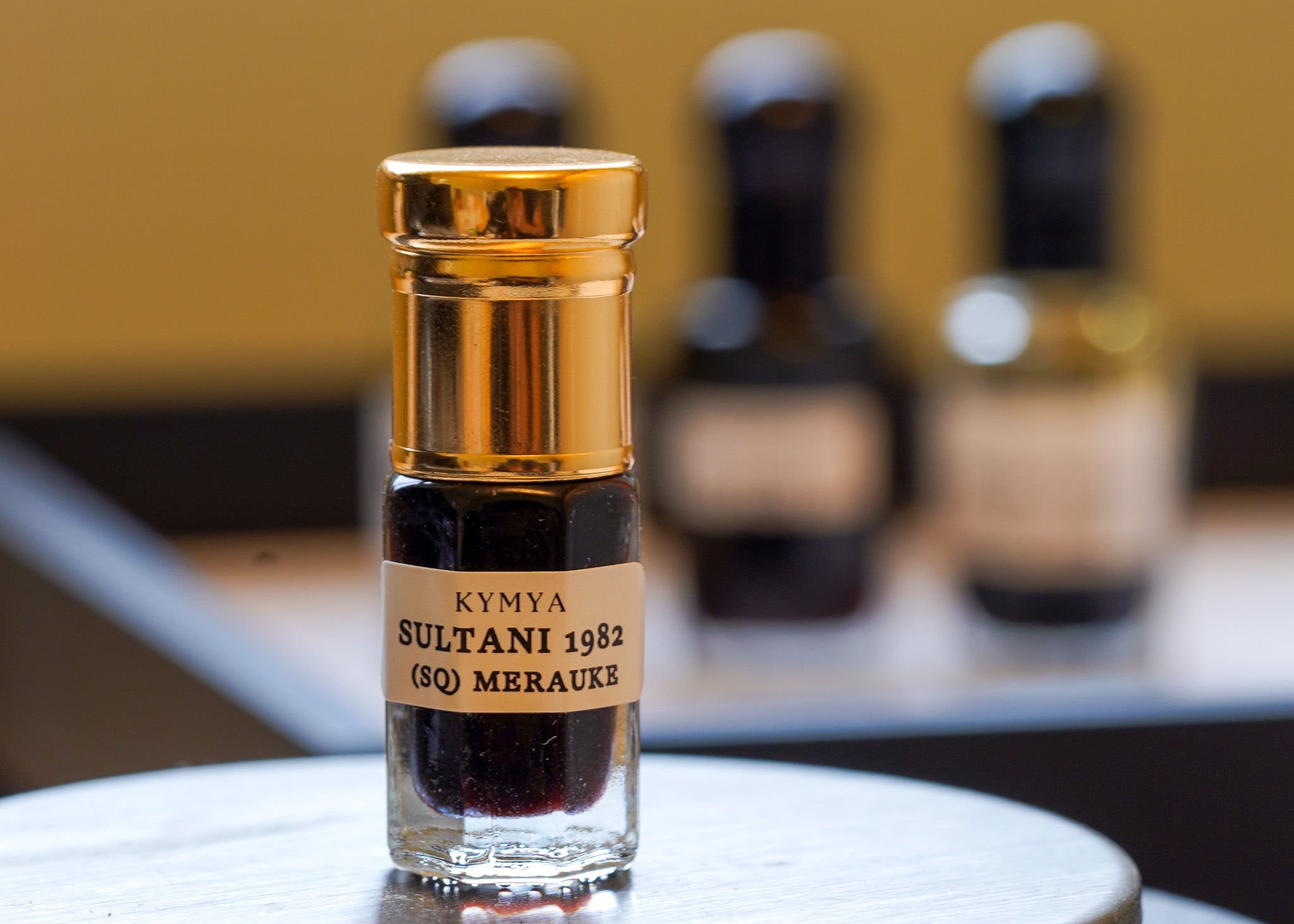 Small bottle labeled 'Kyma Sultani 1982' with gold cap on a blurred background